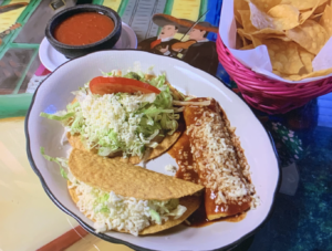 Plate with one taco, one enchilada, and one chalupa from Rey Azteca, served with fresh lettuce, tomatoes, and cheese.